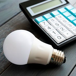 White LED lightbulb next to a calculator on a gray wooden surface.