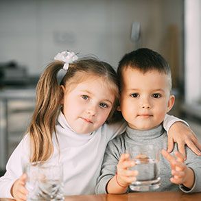 Two children smiling, holding glasses of water, one with arm around the other.