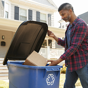 Man putting cardboard into a blue recycling bin in front of a house.
