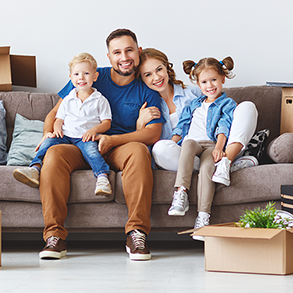 Family of four smiling on a couch, surrounded by moving boxes.