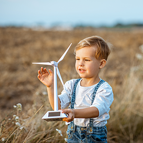 Young child holding a model wind turbine in a field, smiling, sunny day.