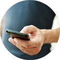 Person holding a black smartphone, touching the screen with their thumb. Blue shirt visible.