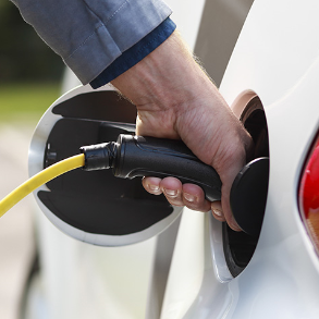 Person plugging yellow charging cable into white electric car.