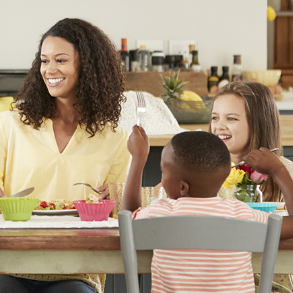 Family smiles while eating at a table in a kitchen.