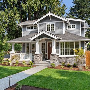 Two-story gray house with porch, stone accents, and manicured lawn.