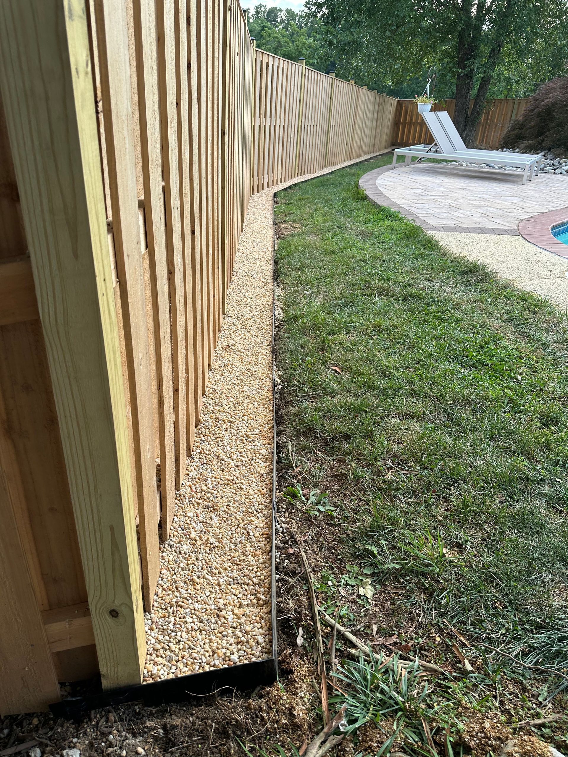 Wooden fence with a gravel bed, separating grass from a pool area.
