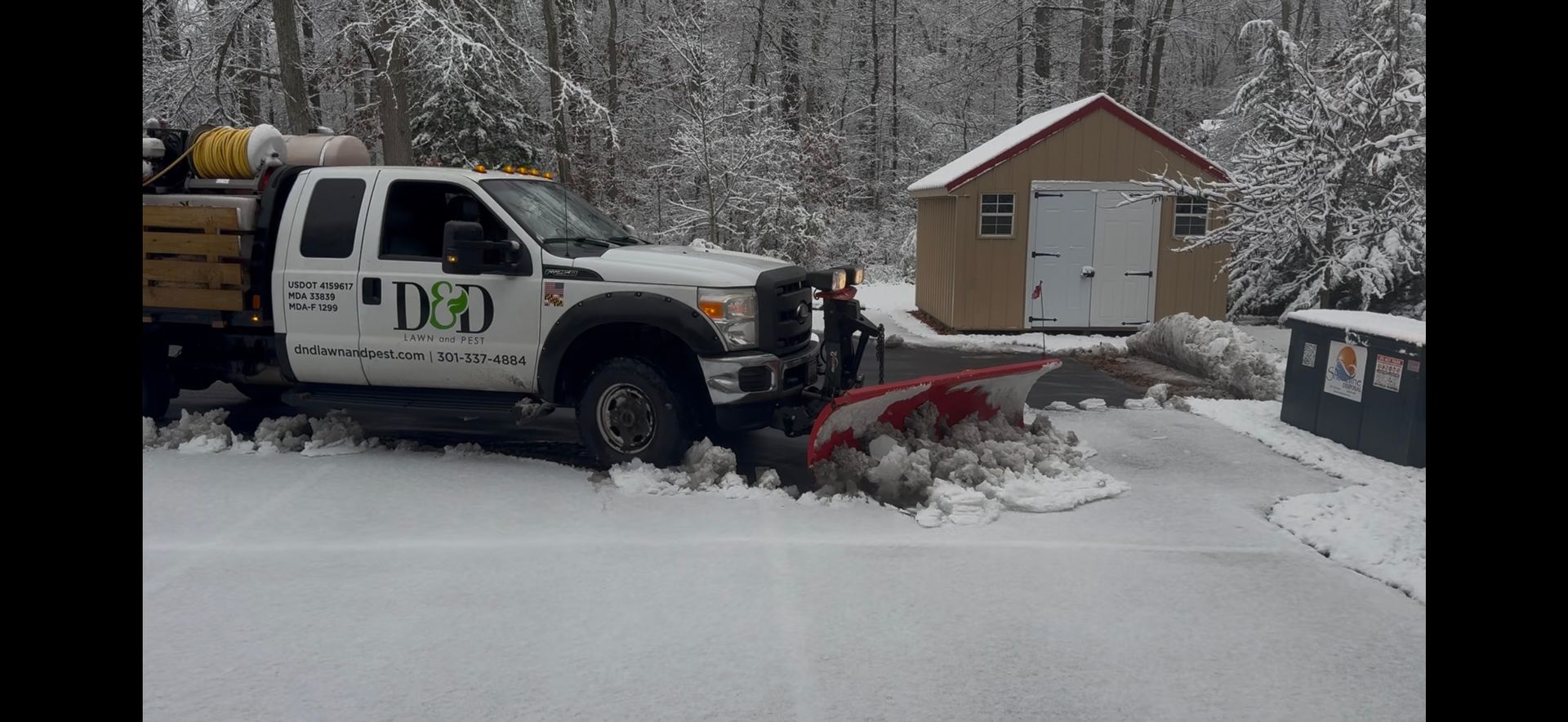Snowplow truck plowing a road on a snowy day; the truck has a front plow and a salt spreader.