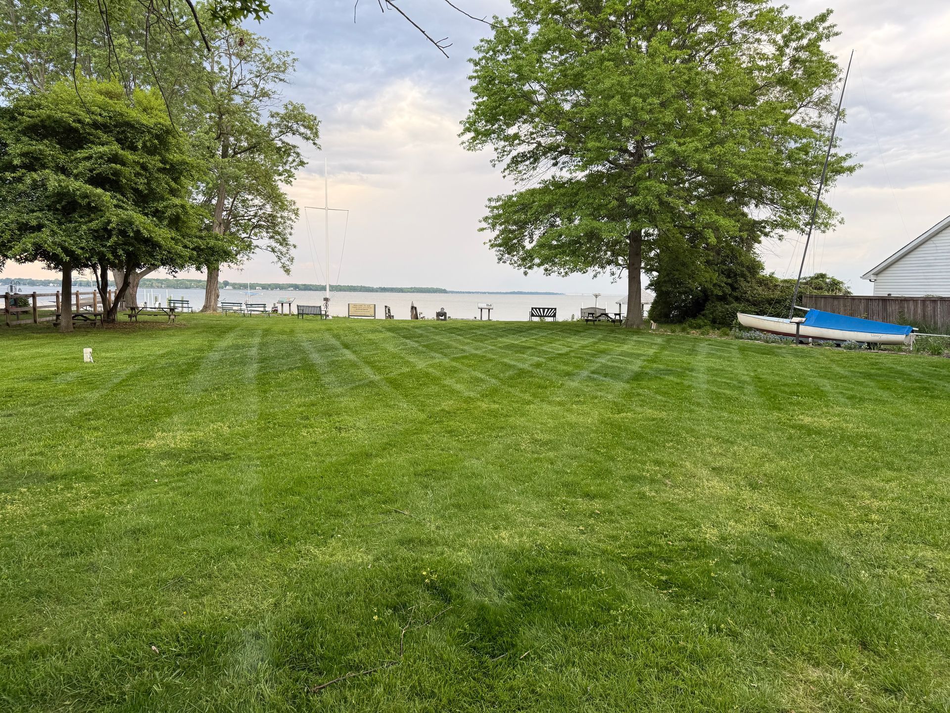 Green lawn slopes down to a lake, with trees on the left and right sides. Sky is overcast.
