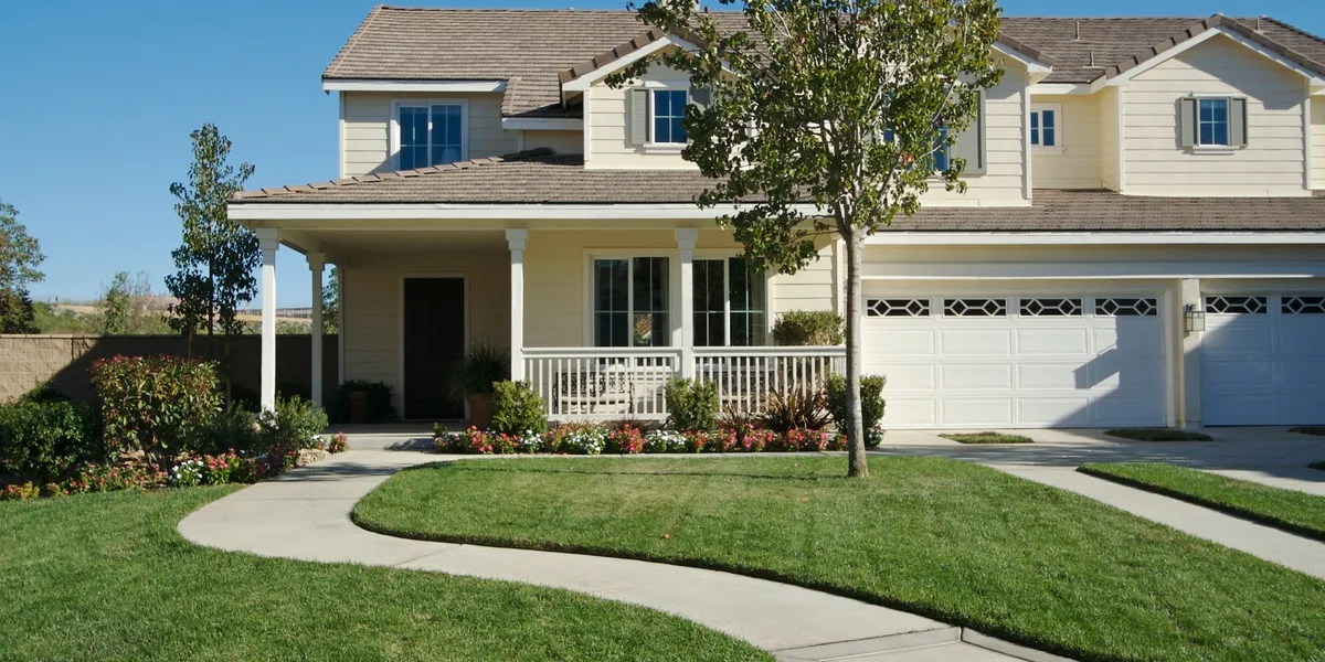 A light yellow two-story house with a green lawn and a curved walkway in front.