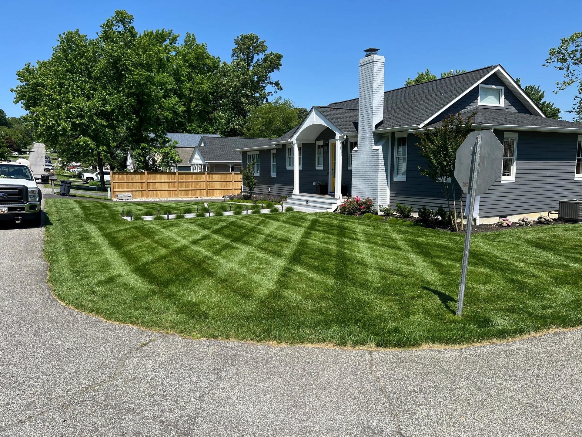 A gray house with a well-maintained lawn, mowed in a crisscross pattern, on a sunny day.
