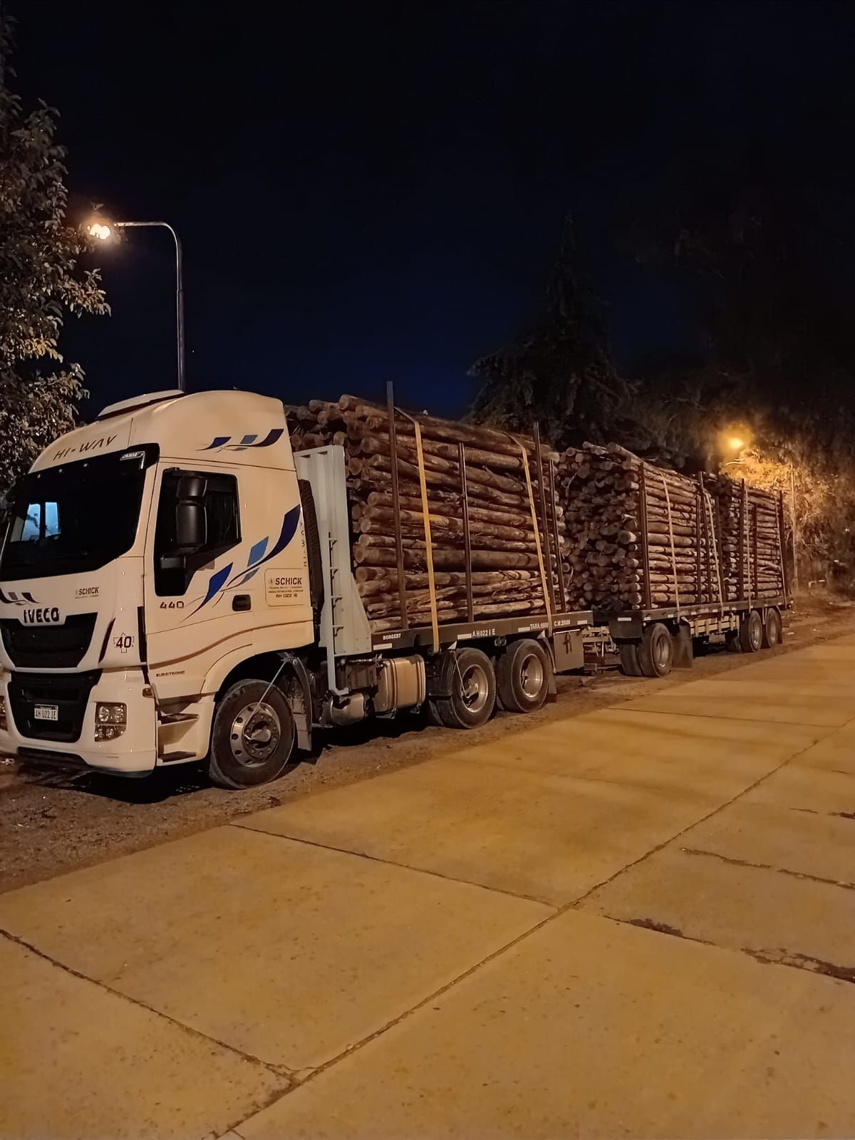 Un camionero con chaleco reflectante está de pie frente a una fila de camiones de reparto azules y blancos estacionados.