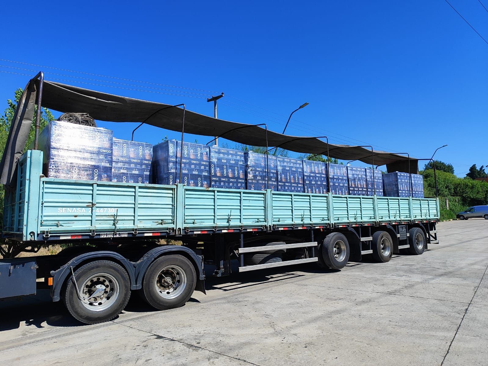 Un camión semirremolque azul transporta cuatro grandes sacos de carga de color beige en una carretera.