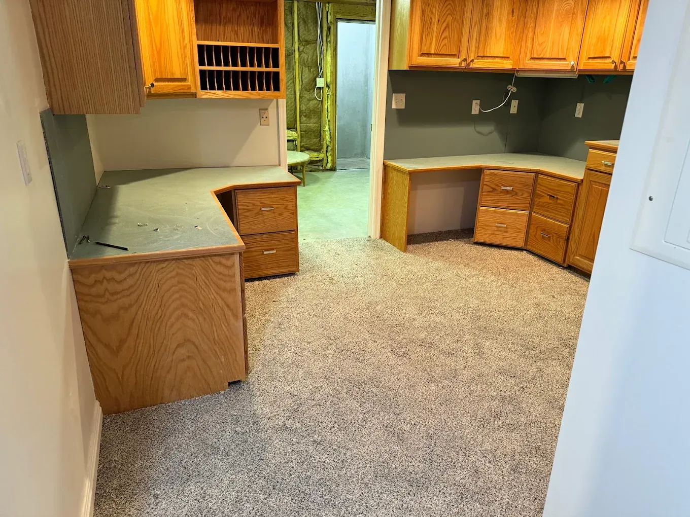 Empty kitchen with wood cabinets, gray countertops, and speckled flooring leading to a doorway.