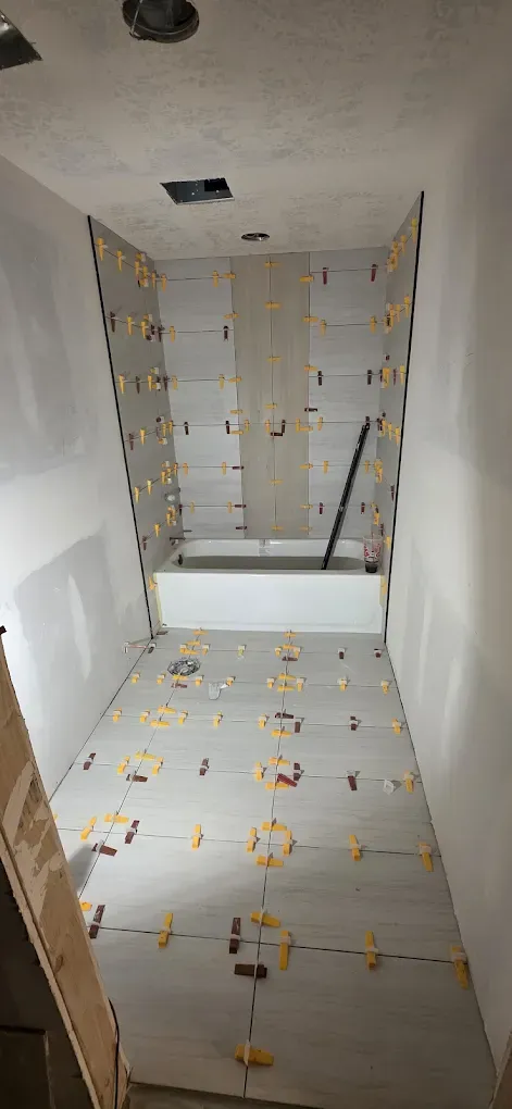 Narrow unfinished hallway with tiled floor and walls, showing exposed wiring and a small opening at the far end