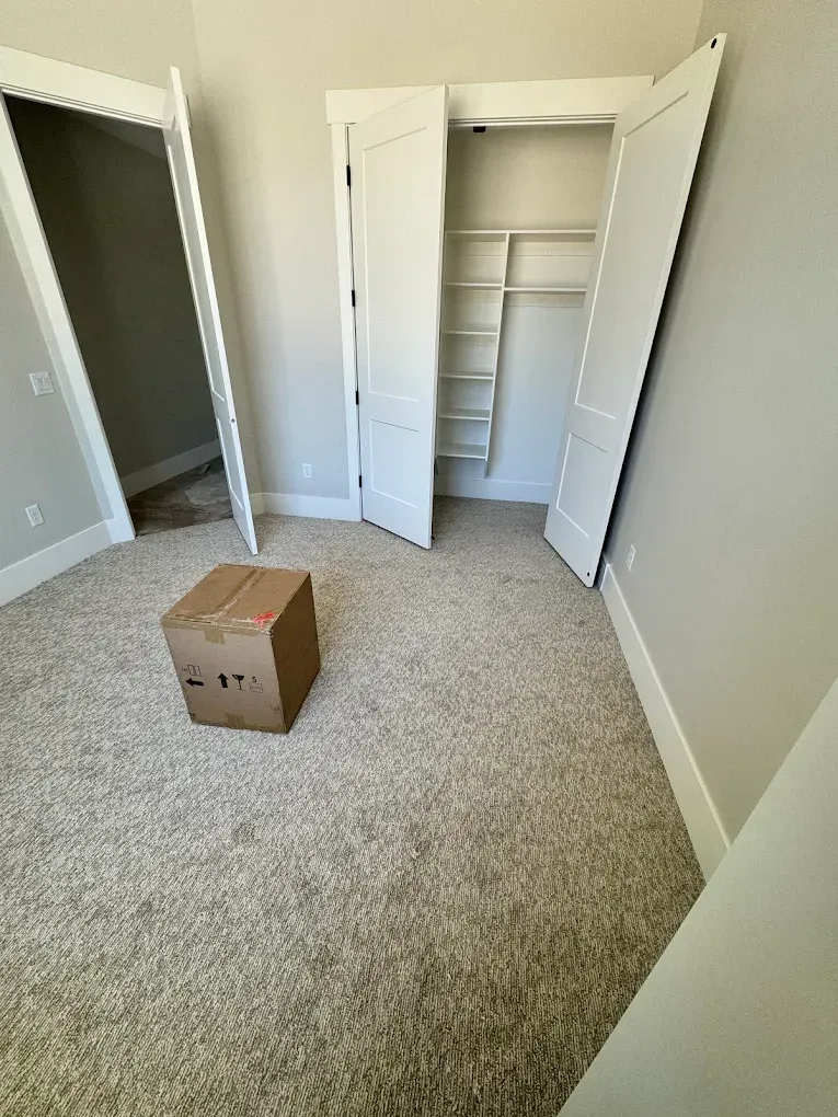 Empty carpeted bedroom with open closet doors and a cardboard box on the floor