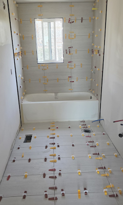 Bathroom under renovation with tiled floor and shower-tub area, lit by a window.