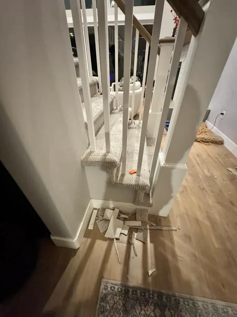 Broken white staircase railing with debris scattered on wooden floor indoors