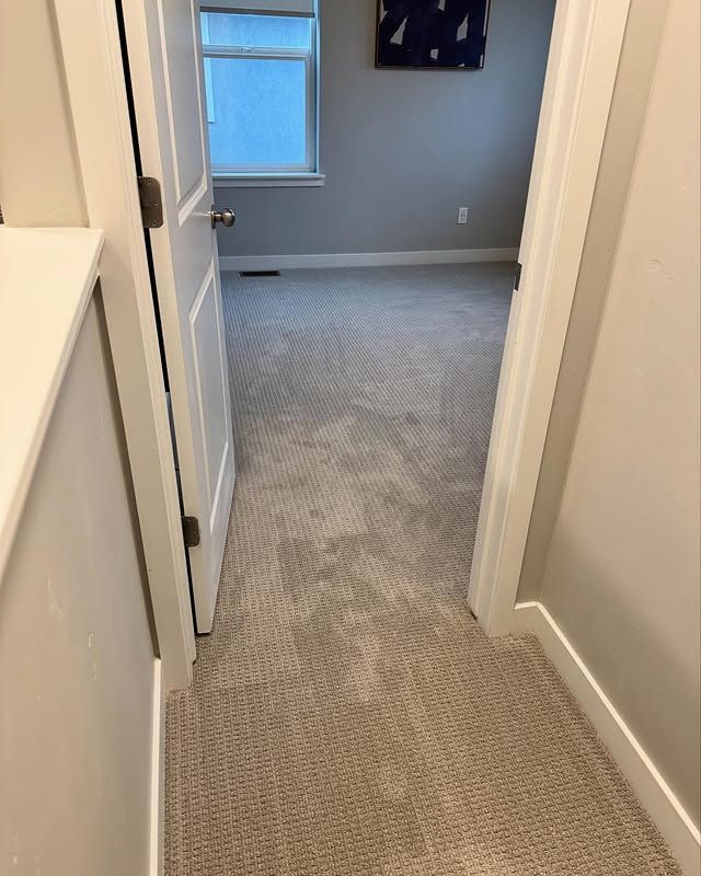 Narrow carpeted hallway leading to a gray bedroom with a window and an open door.