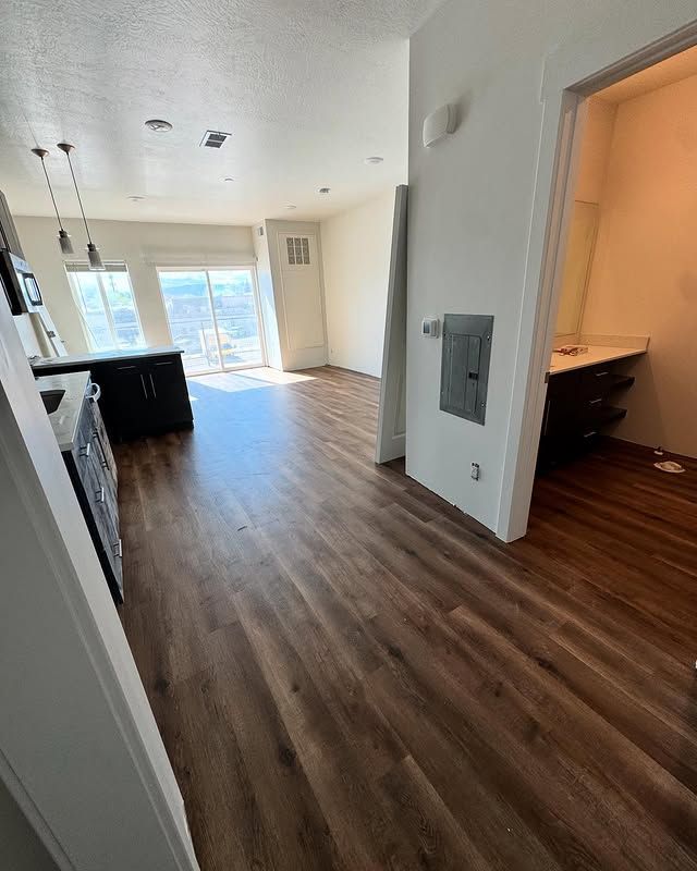 Empty apartment interior with wood floors, kitchen island, and sliding glass doors to a bright balcony