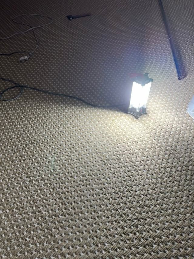 Bright lantern on patterned carpet at night, with a dark cable in the background.