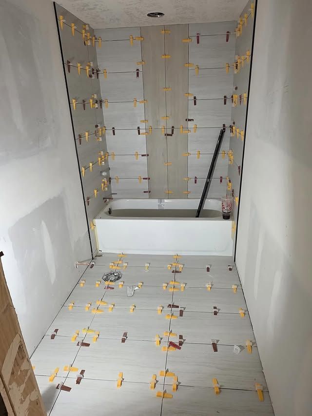 Partially tiled bathroom shower niche with gray wall tiles, yellow spacers, and a white tub base