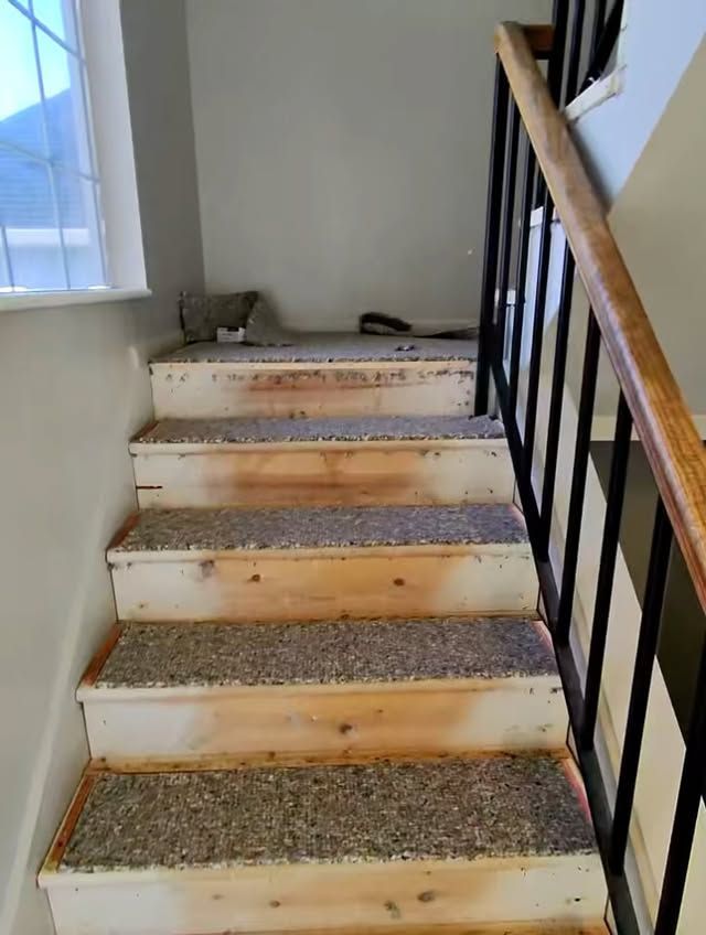 Staircase with worn steps, black railing, and window light from the left