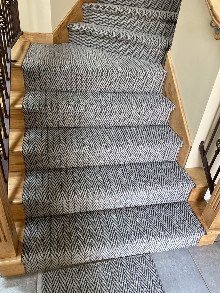 Carpeted staircase with wooden rails and gray runner leading up from a tiled entryway