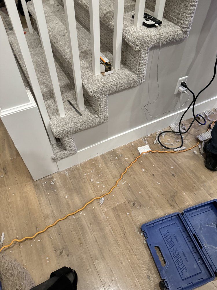 Stairwell with carpeted steps, loose cables, and plastic storage crates on a hardwood floor.