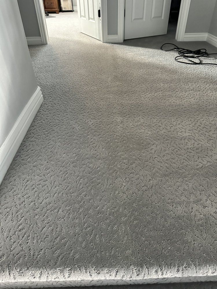 Carpeted hallway with white walls and open doorways, showing a black cord on the floor.