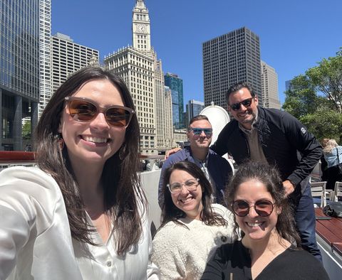 Five people smiling for a selfie on a city bridge with skyline buildings in the background