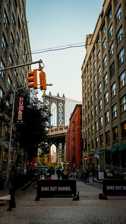 Brooklyn Bridge framed by tall brick buildings on a city street with hanging red lanterns and a barricade sign