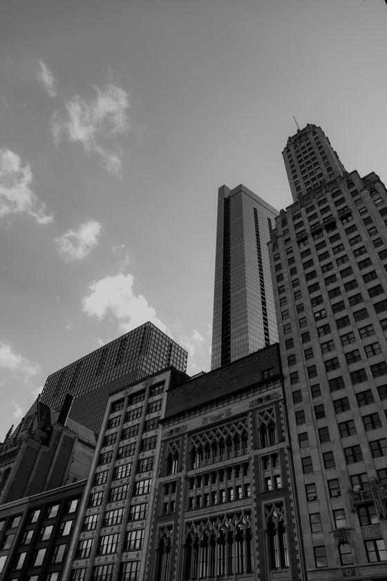 Black-and-white view of tall city skyscrapers against a cloudy sky