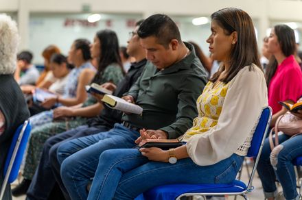 People seated in a conference room, some taking notes during a presentation.