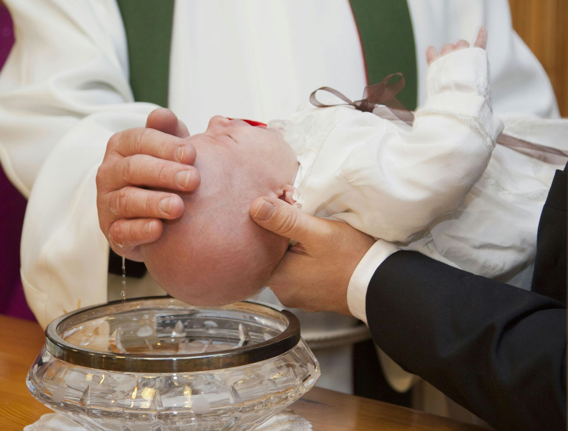 Hands hold a baby’s head over a baptismal basin during a church ceremony