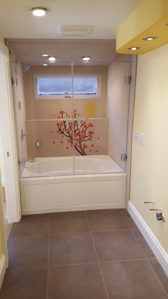 A bathroom with a bathtub and a shower with a tree on the wall.