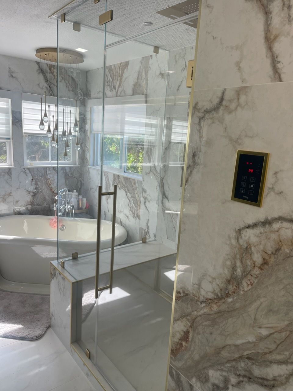 Modern bathroom with glass shower enclosure, marble walls, and a freestanding tub near a window.