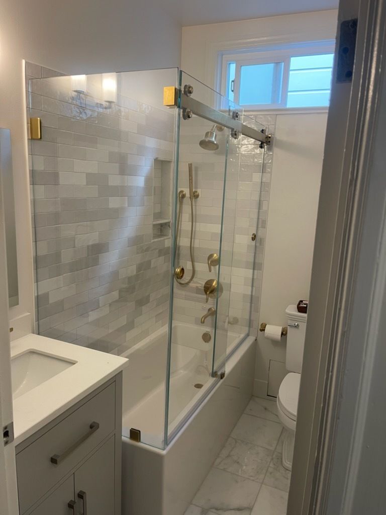Small bathroom with glass shower enclosure, white vanity, toilet, and frosted window.