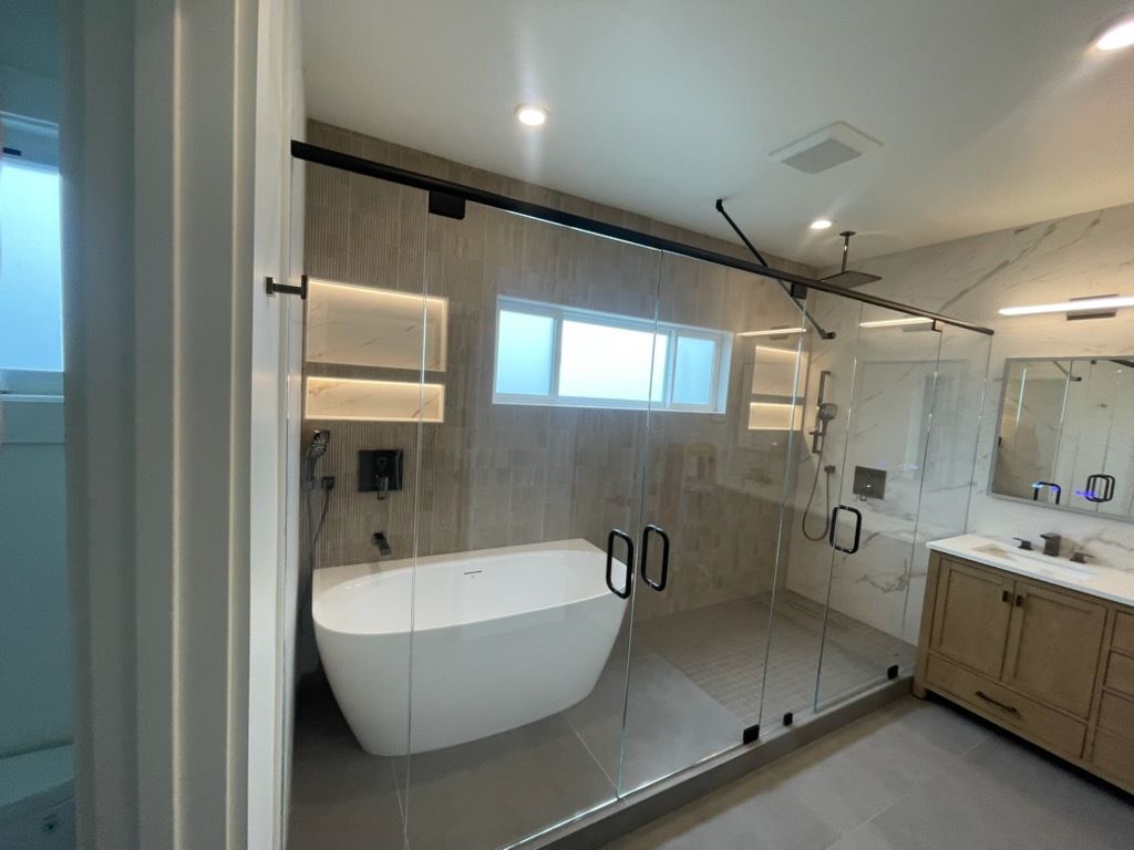 Modern bathroom with freestanding tub, glass shower, and double vanity in gray tile.