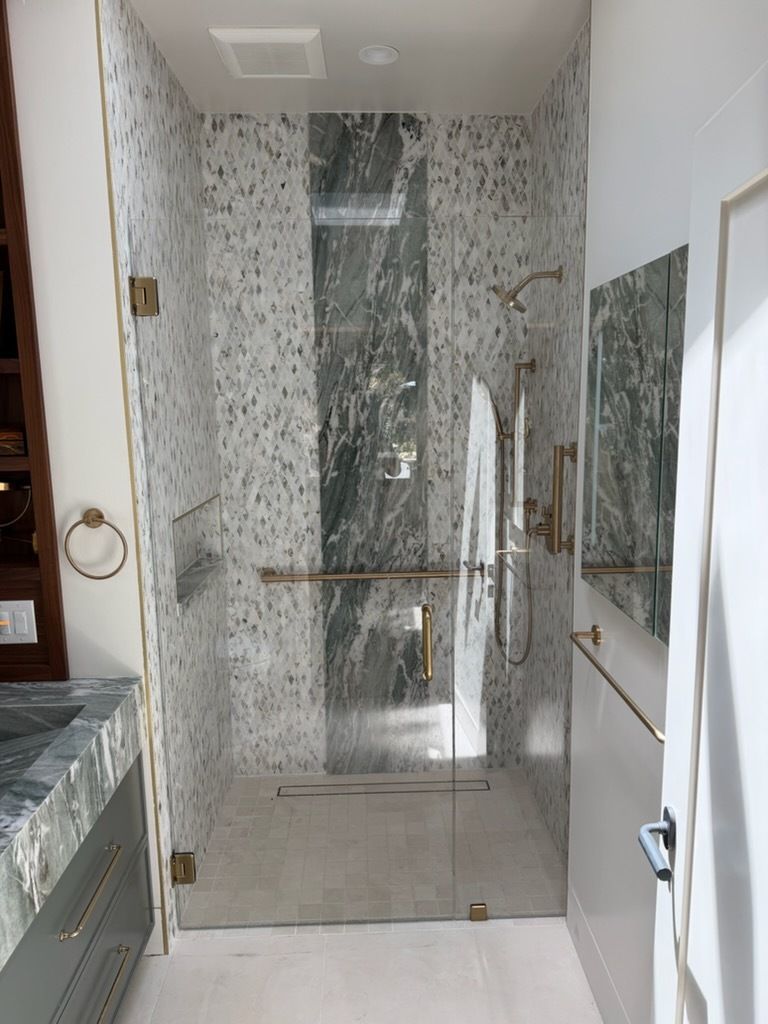 Luxury bathroom shower with glass door, marble walls, grab bars, and built-in bench