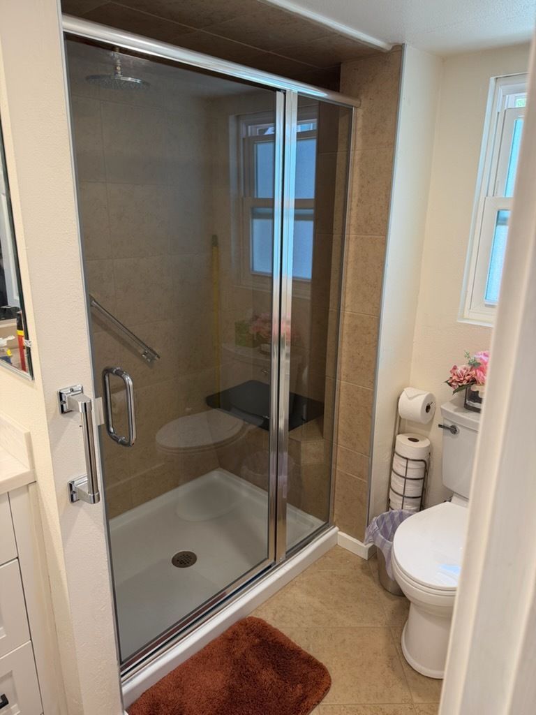 Bathroom with glass-enclosed shower, toilet, and brown bath mat in a small tiled space