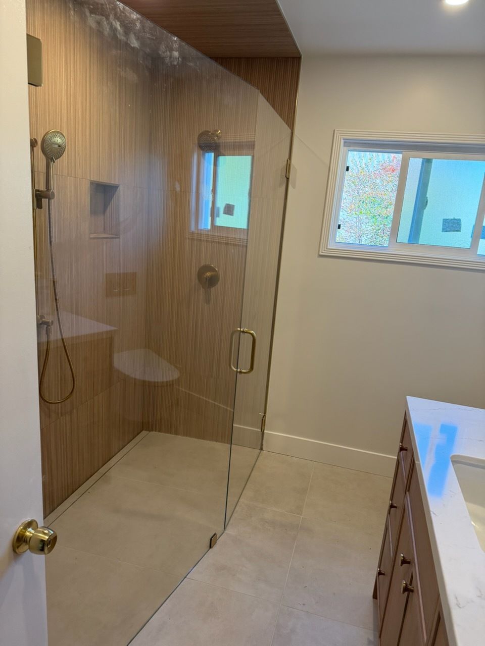 Modern bathroom with glass shower, wood-look wall tile, window, and vanity drawers