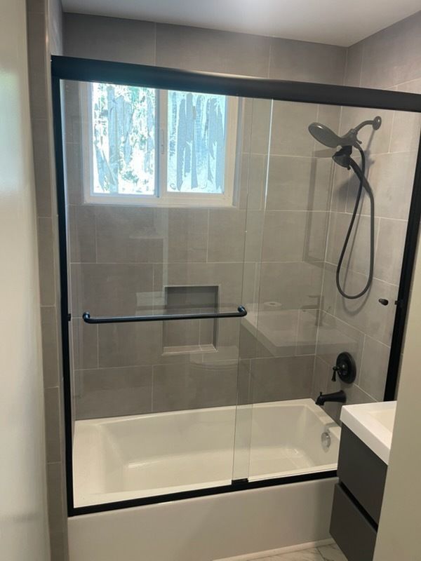 Bathroom shower with glass enclosure, tiled walls, and a window above the tub.
