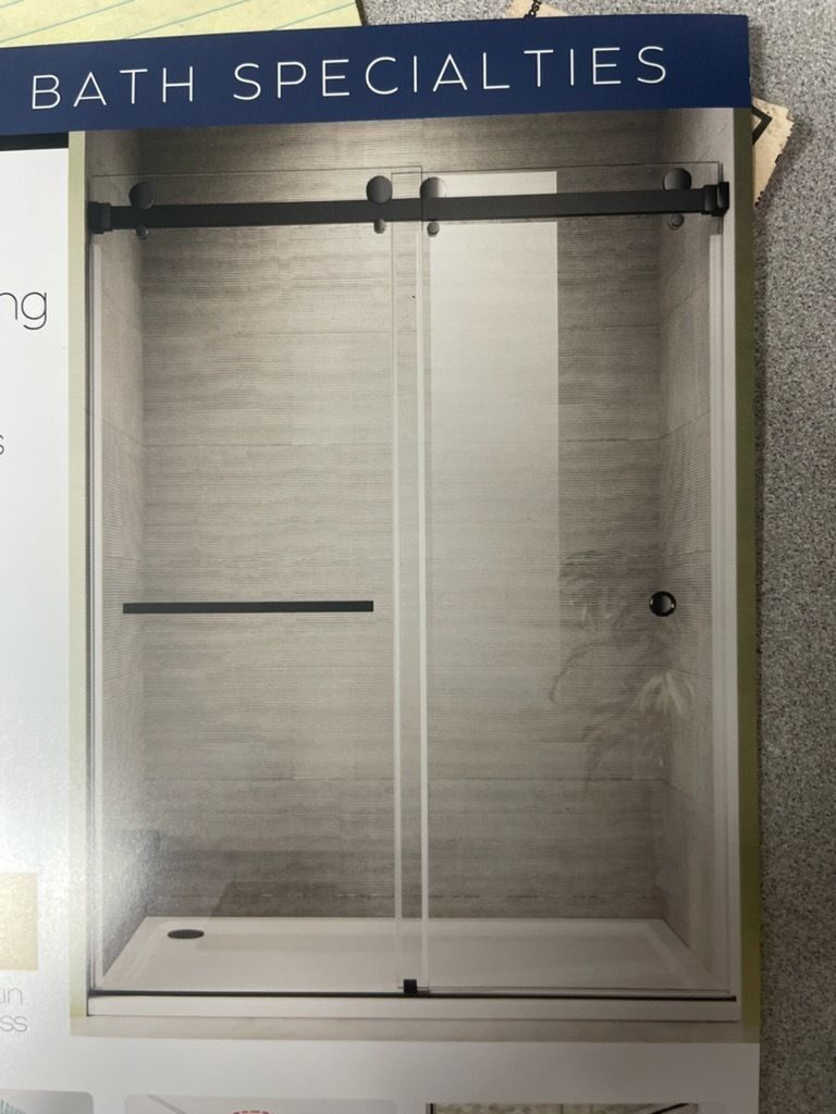 Glass shower enclosure display with black hardware in a bathroom showroom, under a Bath Specialties sign
