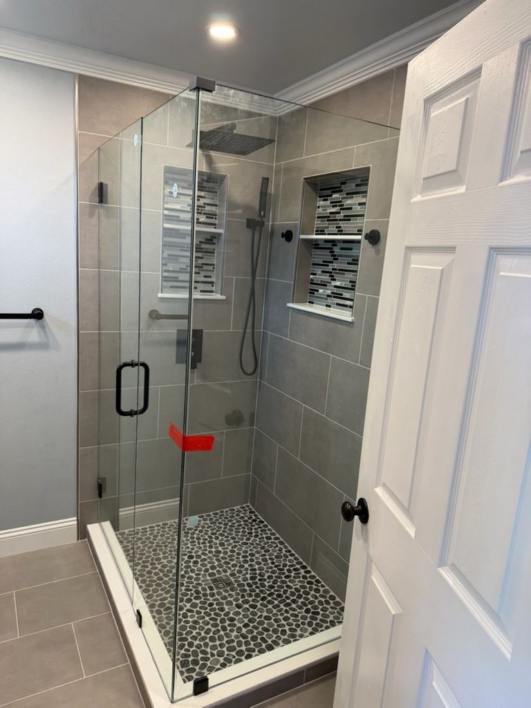 Modern bathroom with glass-enclosed shower, gray tile, and pebble-pattern shower floor.