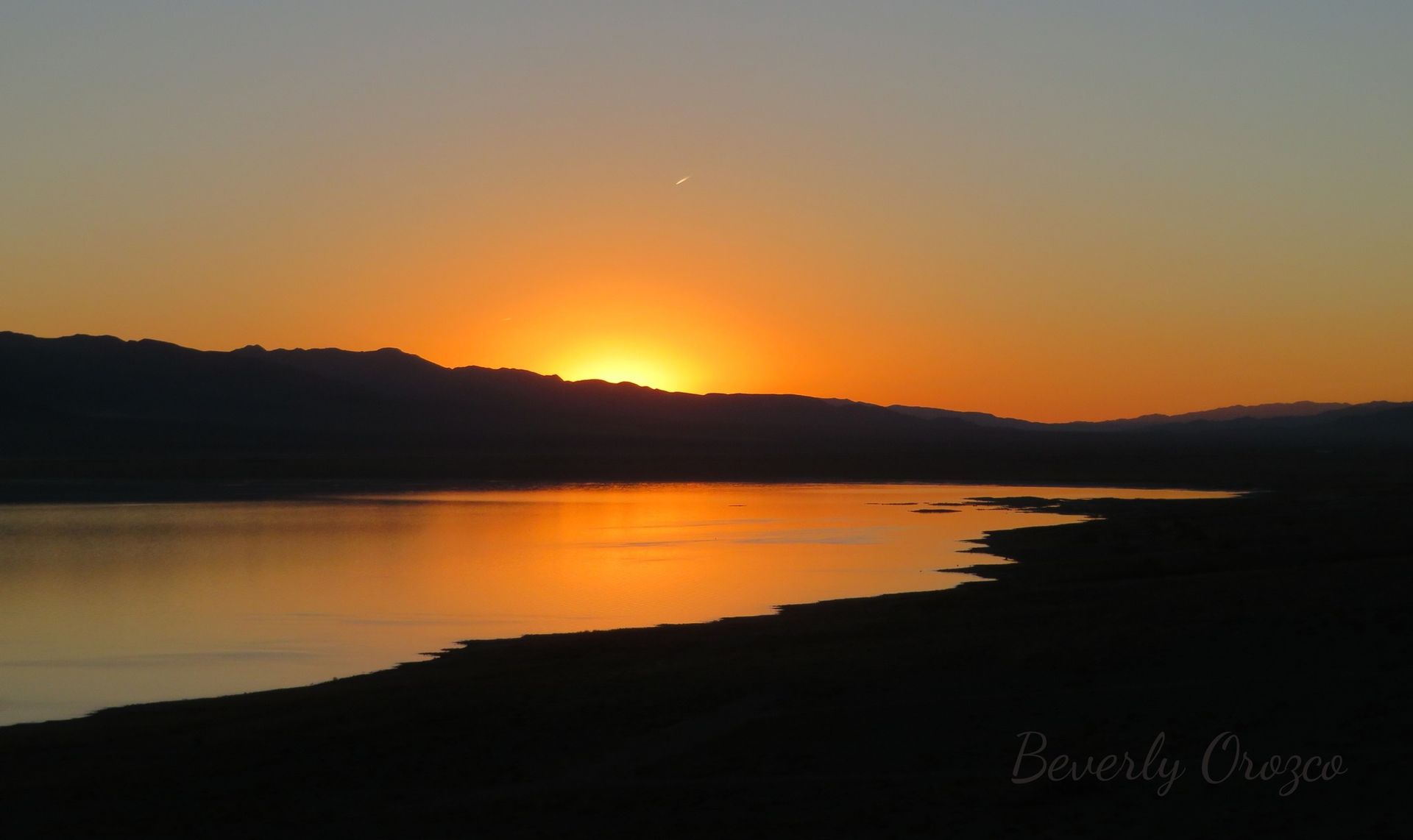The sun is setting over a lake with mountains in the background