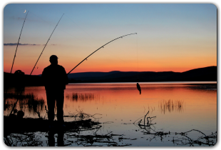 A man is fishing in a lake at sunset