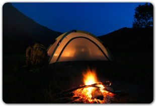 A tent is lit up next to a campfire at night