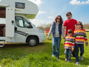 A family is standing in front of a rv in a field.