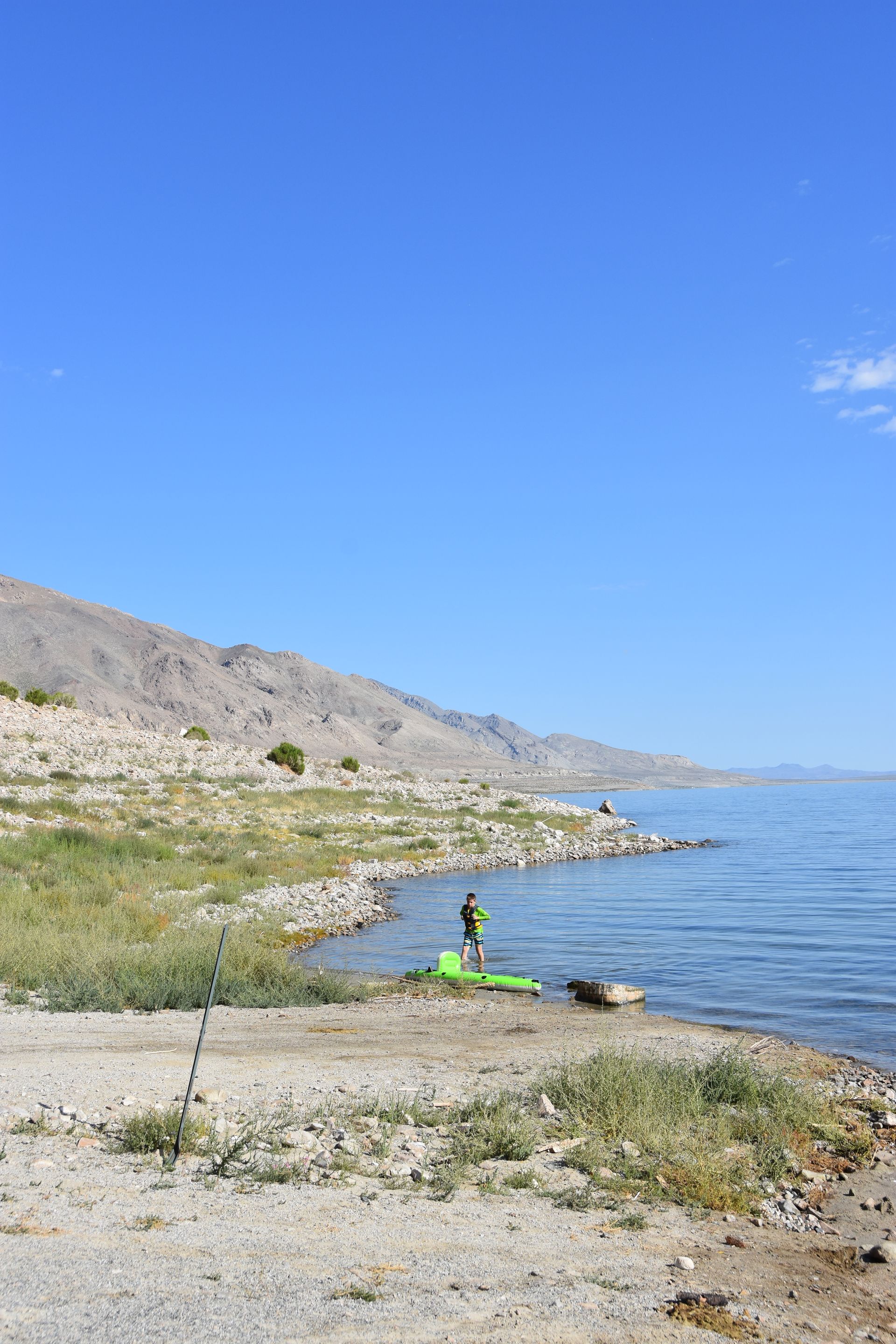 A person is standing on the shore of a lake with mountains in the background.