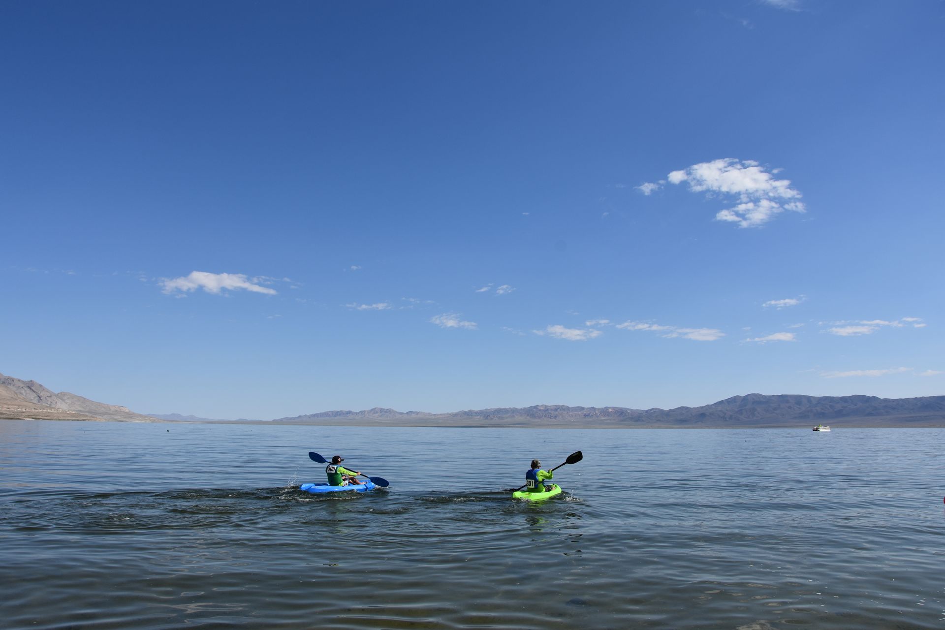Two people are kayaking on a lake with mountains in the background.
